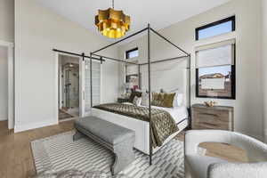 Bedroom with a barn door, wood finished floors, a chandelier, and connected bathroom