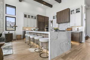 Kitchen with decorative backsplash, glass insert cabinets, white cabinetry, a high ceiling, and beam ceiling