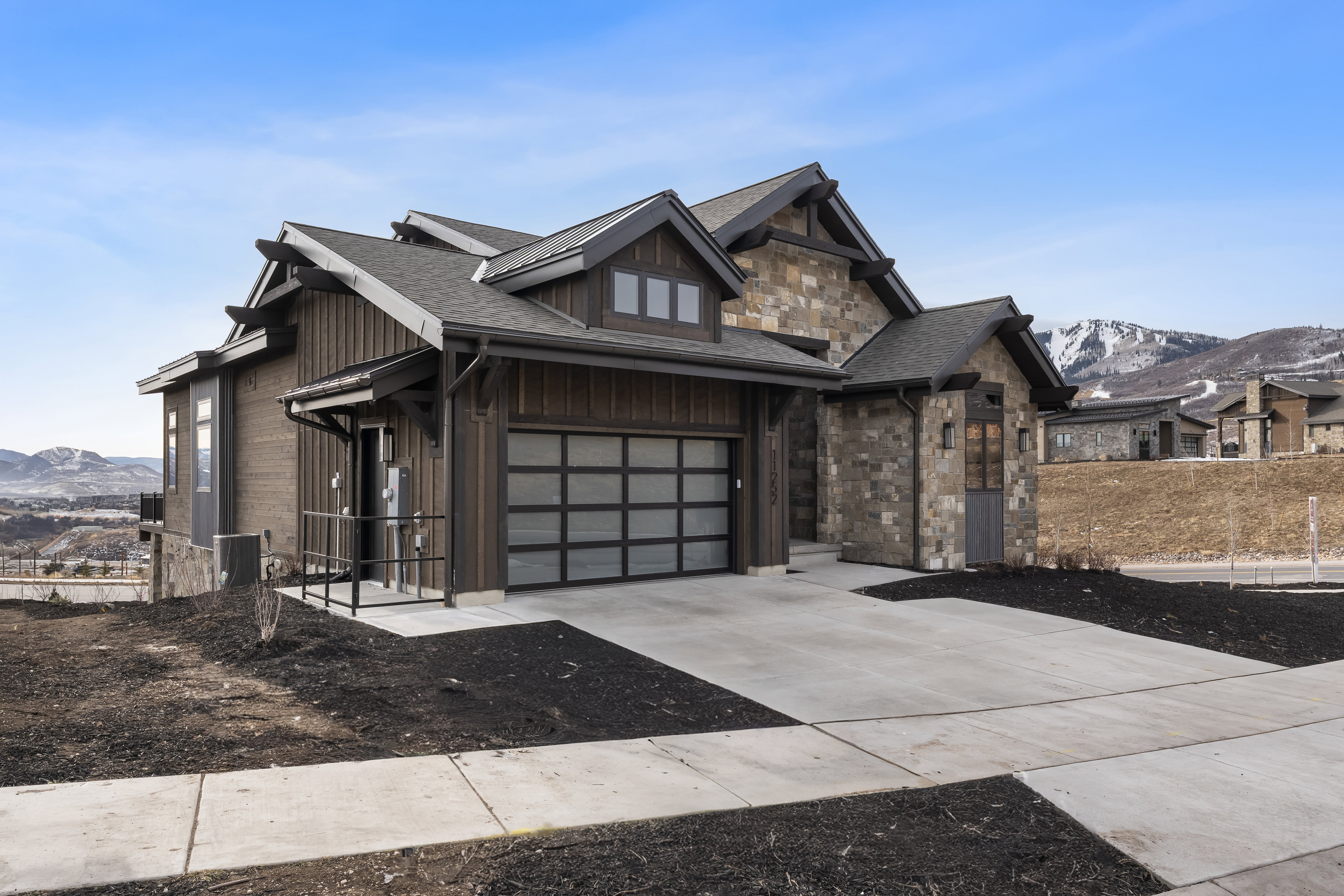 View of front facade with a mountain view, stone siding, concrete driveway, a garage, and roof with shingles
