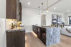 Kitchen featuring dark brown cabinets, a peninsula, light stone counters, light wood-type flooring, and decorative light fixtures