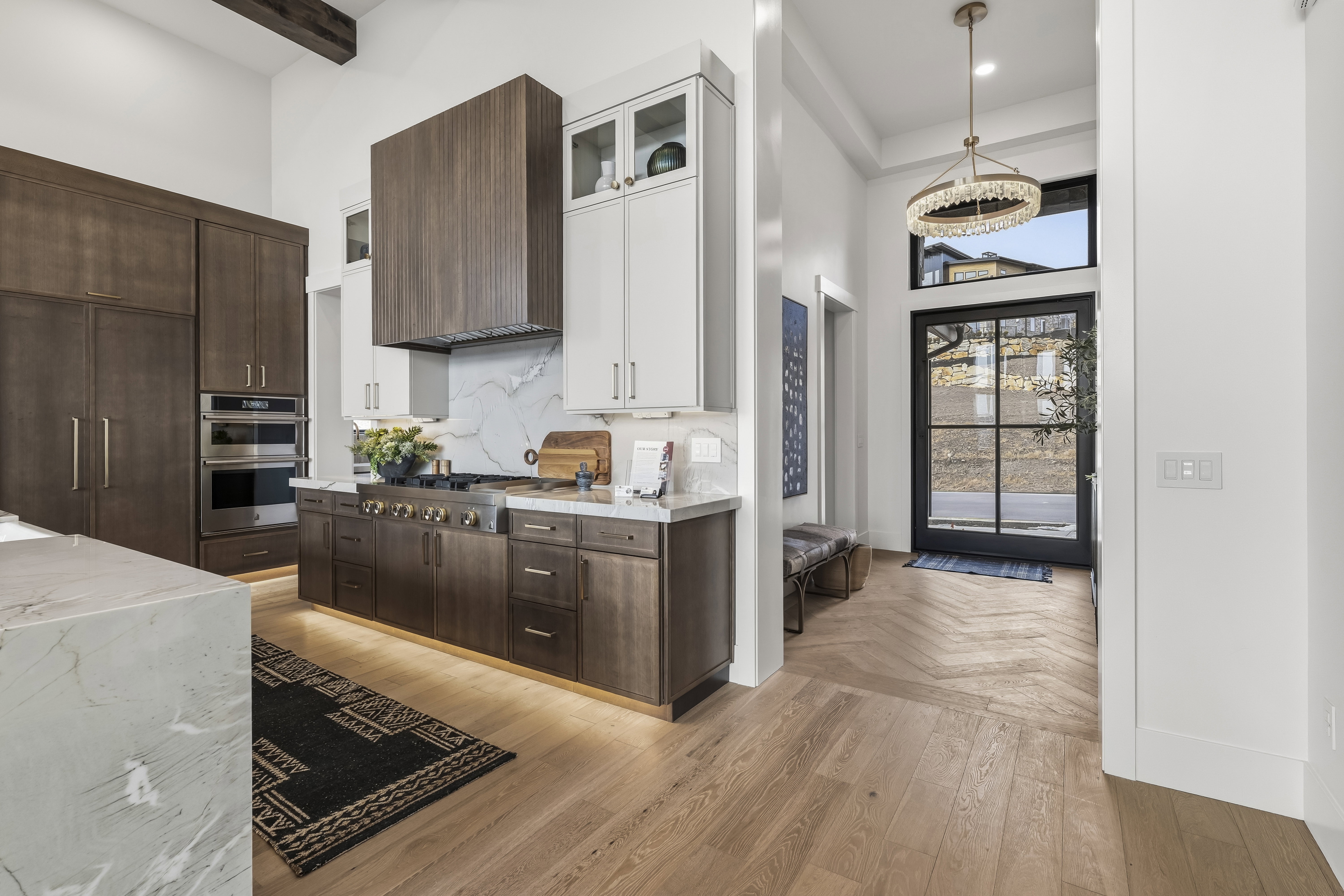 Kitchen featuring dark brown cabinetry, a high ceiling, glass insert cabinets, light wood-style floors, and light stone counters