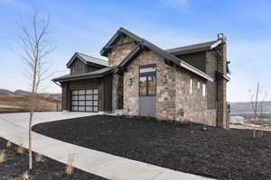 View of front of home with concrete driveway, a mountain view, stone siding, a metal roof, and a standing seam roof