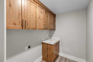 Laundry area with electric dryer hookup, cabinet space, and light wood-style floors