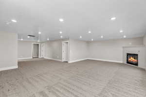Unfurnished living room with a glass covered fireplace, recessed lighting, and light colored carpet