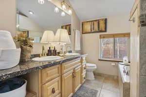 Bathroom with double vanity, tiled tub, vaulted ceiling, and light tile patterned floors