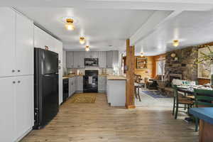 Kitchen featuring open floor plan, a fireplace, black appliances, light wood-style flooring, and gray cabinetry