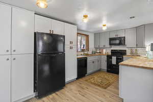 Kitchen with wood counters, black appliances, light wood finished floors, a textured ceiling, and gray cabinetry