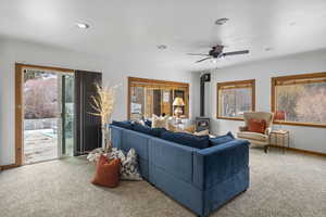 Carpeted living area with a wood stove, plenty of natural light, a ceiling fan, and recessed lighting