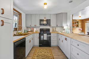 Kitchen with black appliances, plenty of natural light, butcher block countertops, light wood-style floors, and wooden walls