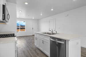 Kitchen with light countertops, appliances with stainless steel finishes, white cabinets, dark wood-type flooring, and a center island with sink