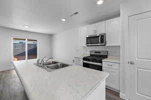 Kitchen featuring white cabinetry, light countertops, appliances with stainless steel finishes, a center island with sink, and recessed lighting