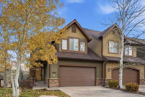View of front of home featuring stone siding, board and batten siding, a garage, roof with shingles, and concrete driveway