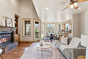 Living room with light wood-style floors, built in shelves, a tile fireplace, a ceiling fan, and a chandelier