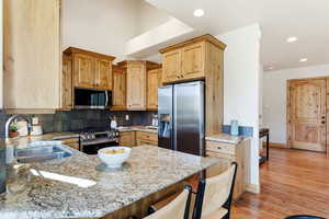 Kitchen featuring light stone counters, a breakfast bar, appliances with stainless steel finishes, a peninsula, and light wood finished floors