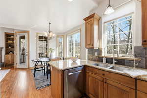 Kitchen with pendant lighting, dishwasher, brown cabinetry, and light stone counters