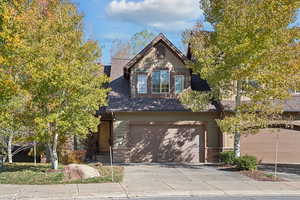 View of front of house featuring stone siding, driveway, an attached garage, and a shingled roof