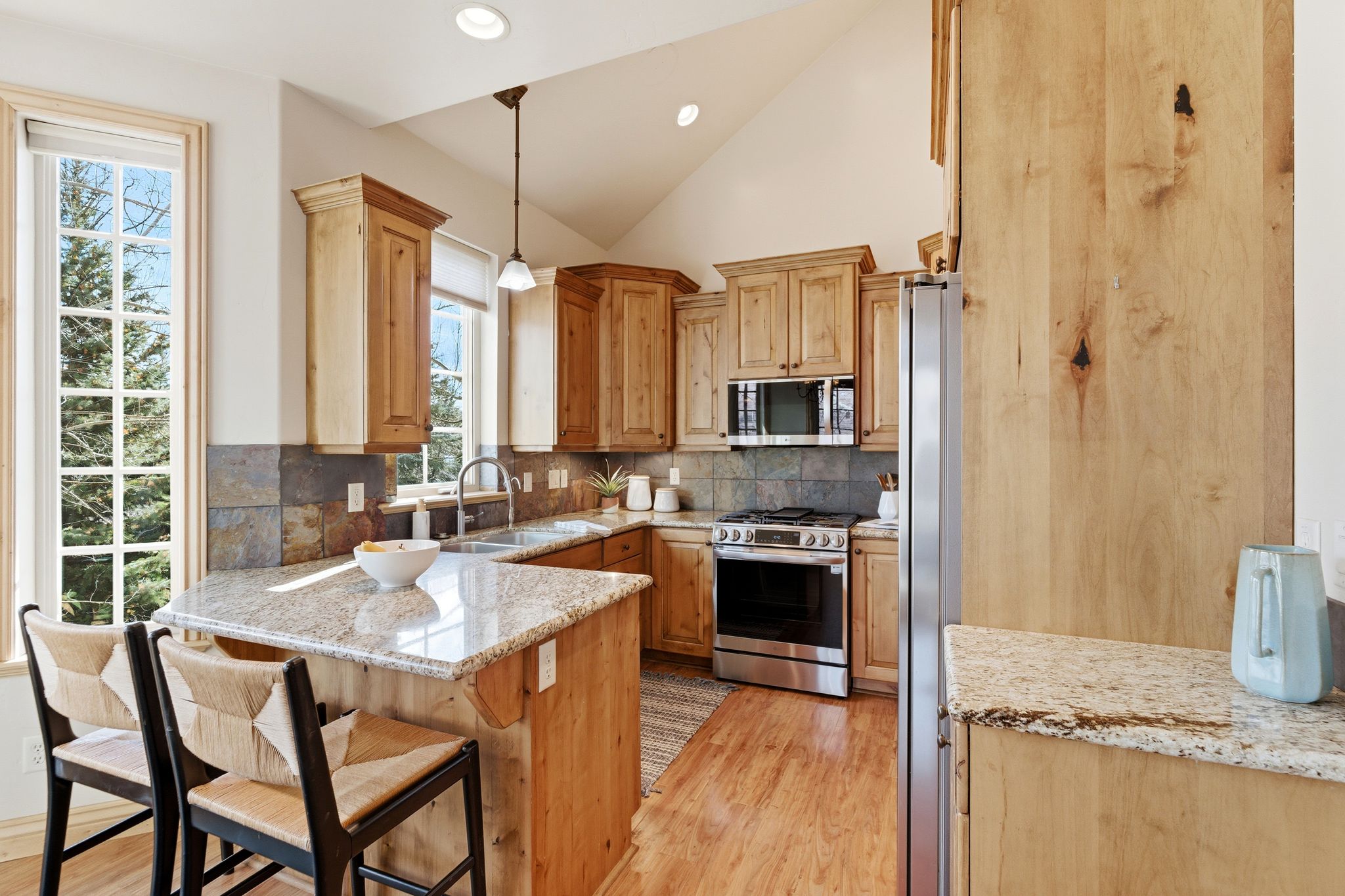 Kitchen featuring light stone counters, pendant lighting, appliances with stainless steel finishes, light wood-style flooring, and decorative backsplash