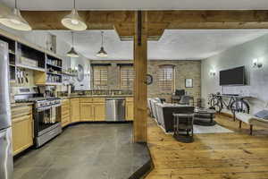 Kitchen with brick wall, stainless steel appliances, open floor plan, decorative light fixtures, and open shelves