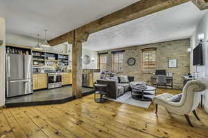 Living room featuring brick wall, dark wood-style floors, and beam ceiling