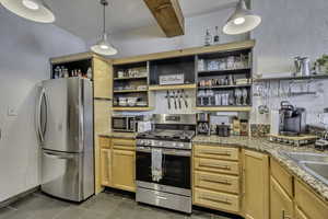 Kitchen with appliances with stainless steel finishes, light brown cabinets, light stone counters, open shelves, and dark tile patterned flooring