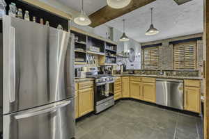Kitchen with appliances with stainless steel finishes, open shelves, light stone counters, and hanging light fixtures