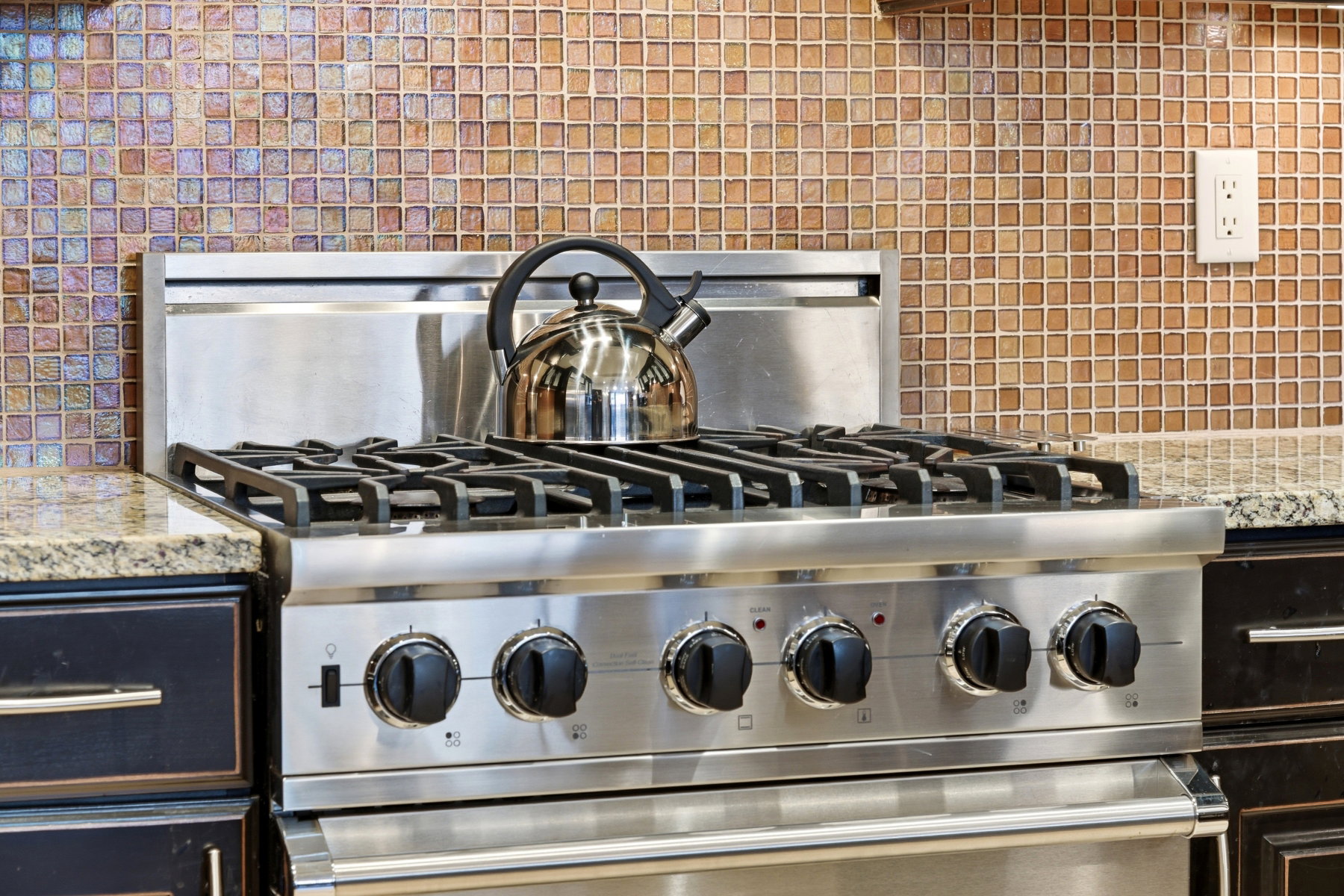Kitchen view of light stone countertops, stainless steel range, and backsplash