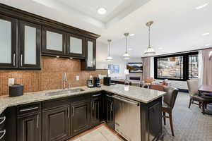Kitchen featuring light stone counters, decorative backsplash, decorative light fixtures, dark cabinetry, and dishwasher