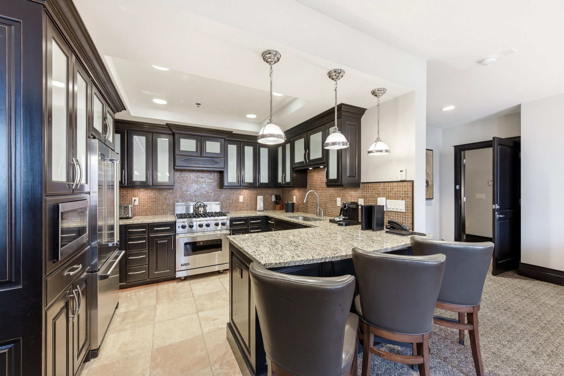 Kitchen featuring decorative light fixtures, a kitchen bar, high end appliances, light stone counters, and glass insert cabinets