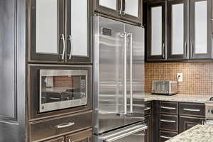 Kitchen with glass insert cabinets, appliances with stainless steel finishes, light stone counters, and tasteful backsplash