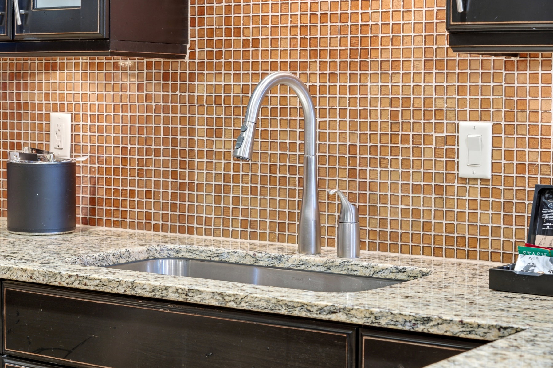 Kitchen view of backsplash, dark brown cabinetry, and light stone counters