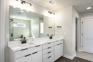 Full bath featuring double vanity, recessed lighting, a spacious closet, and dark tile patterned flooring