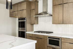 Kitchen featuring wall chimney exhaust hood, appliances with stainless steel finishes, light stone countertops, tasteful backsplash, and modern cabinets