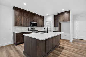 Kitchen featuring tasteful backsplash, dark brown cabinets, stainless steel appliances, a kitchen island with sink, and recessed lighting