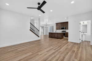Unfurnished living room featuring stairway, recessed lighting, light wood-type flooring, ceiling fan, and a chandelier