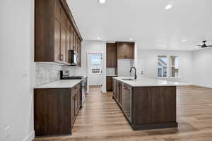 Kitchen with appliances with stainless steel finishes, light stone countertops, dark brown cabinetry, a kitchen island with sink, and recessed lighting