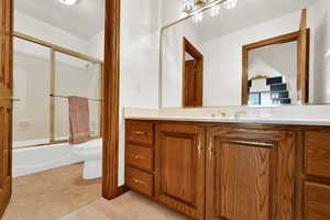 Bathroom with vanity, bath / shower combo with glass door, and light tile patterned floors