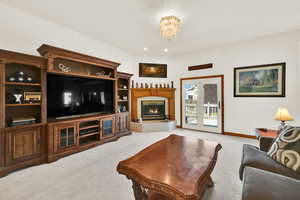 Living room with light colored carpet, recessed lighting, a lit fireplace, and a chandelier