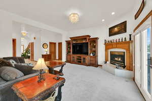 Living area with a glass covered fireplace, light colored carpet, recessed lighting, and a chandelier