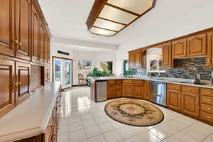 Kitchen featuring brown cabinets, light countertops, light tile patterned flooring, a peninsula, and healthy amount of natural light
