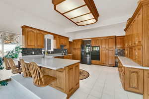 Kitchen with brown cabinetry, a peninsula, black appliances, and backsplash