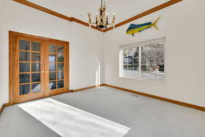 Carpeted spare room with a chandelier, ornamental molding, and french doors