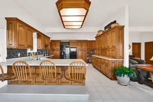 Kitchen with brown cabinetry, light countertops, a peninsula, and backsplash