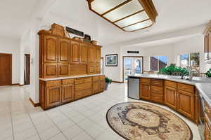 Kitchen featuring brown cabinets, light countertops, a peninsula, stainless steel dishwasher, and light tile patterned floors