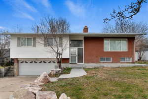View of front of property featuring a front yard, brick siding, concrete driveway, a chimney, and a garage