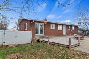 Rear view of house featuring a gate, a chimney, a wooden deck, french doors, and brick siding
