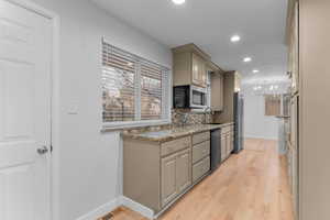 Kitchen featuring light stone counters, decorative light fixtures, backsplash, light wood-type flooring, and stainless steel appliances