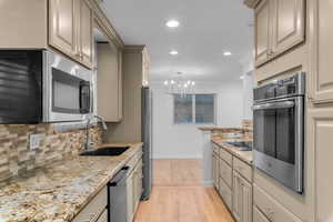 Kitchen featuring hanging light fixtures, light stone countertops, stainless steel appliances, decorative backsplash, and light wood-type flooring