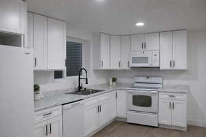 Kitchen with white appliances, white cabinets, light wood-style flooring, light stone counters, and recessed lighting
