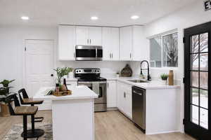 Kitchen with stainless steel appliances, white cabinets, light stone countertops, a kitchen island, and recessed lighting