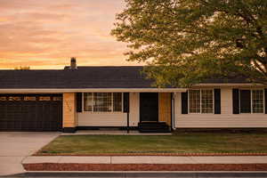 View of front facade with driveway, an attached garage, a chimney, a lawn, and covered porch